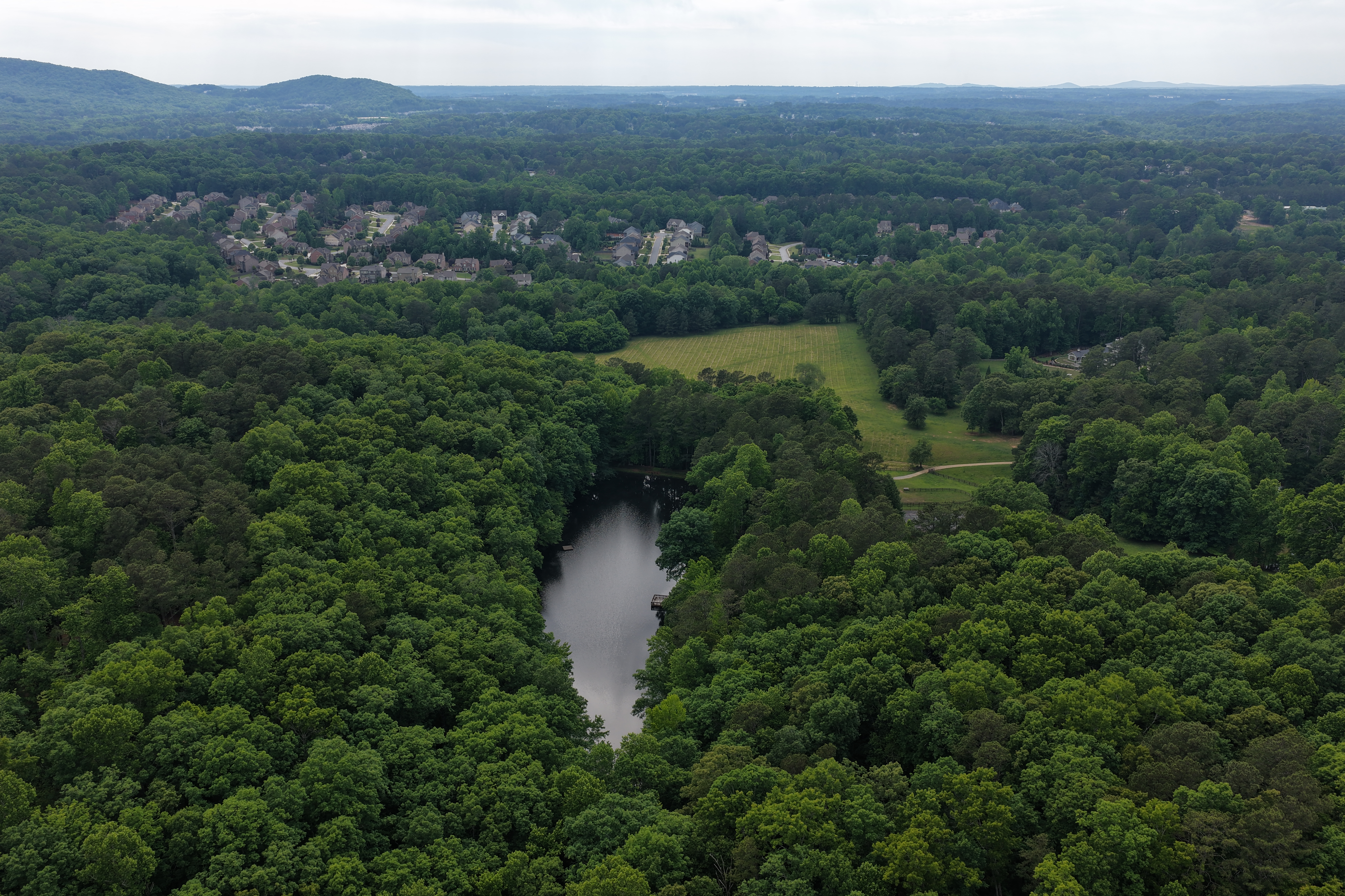 Maximum altitude — lake, golf course, and the estate barely visible in an unbroken sea of Atlanta canopy