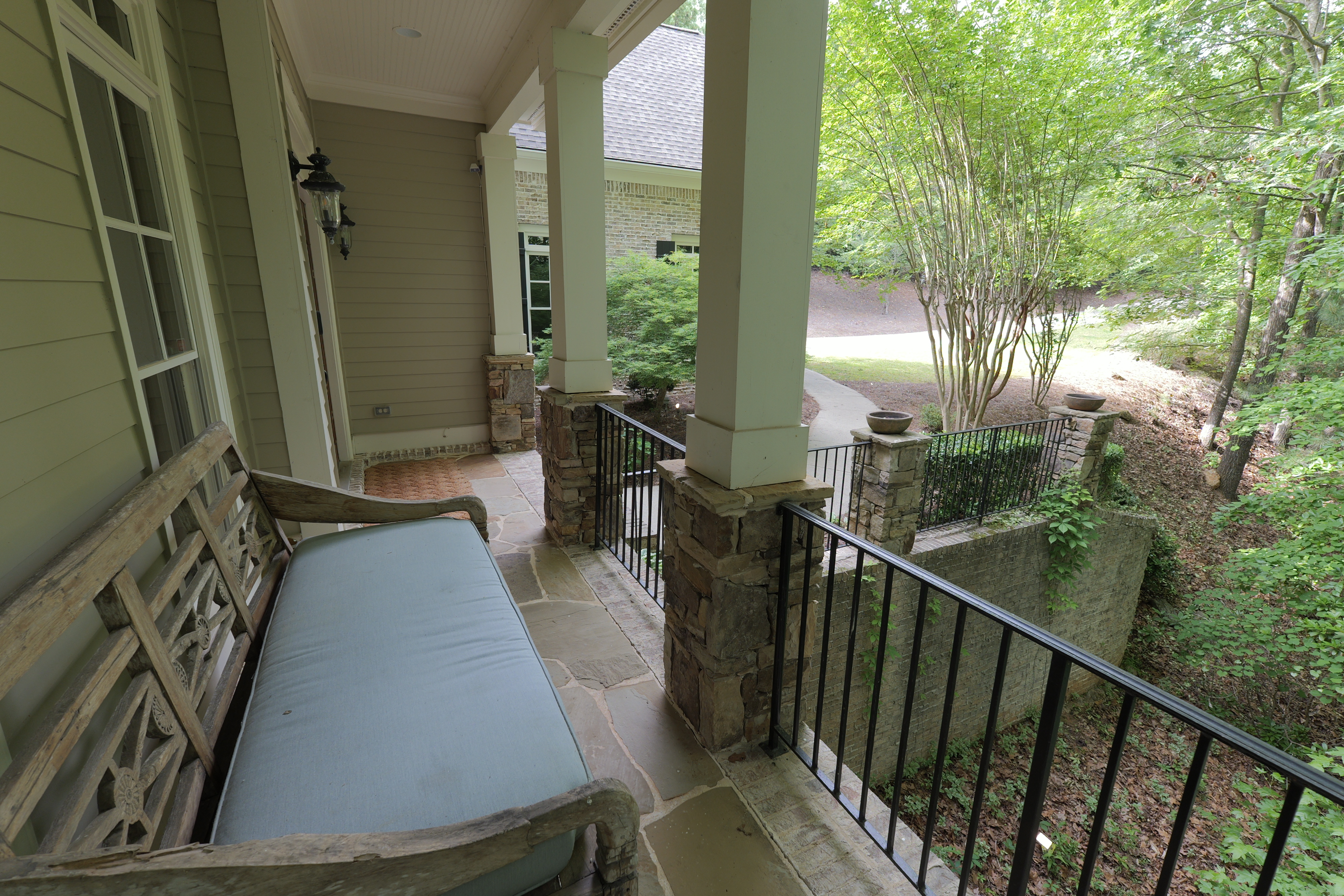 Porch looking out — antique bench, stone floor, driveway through the trees