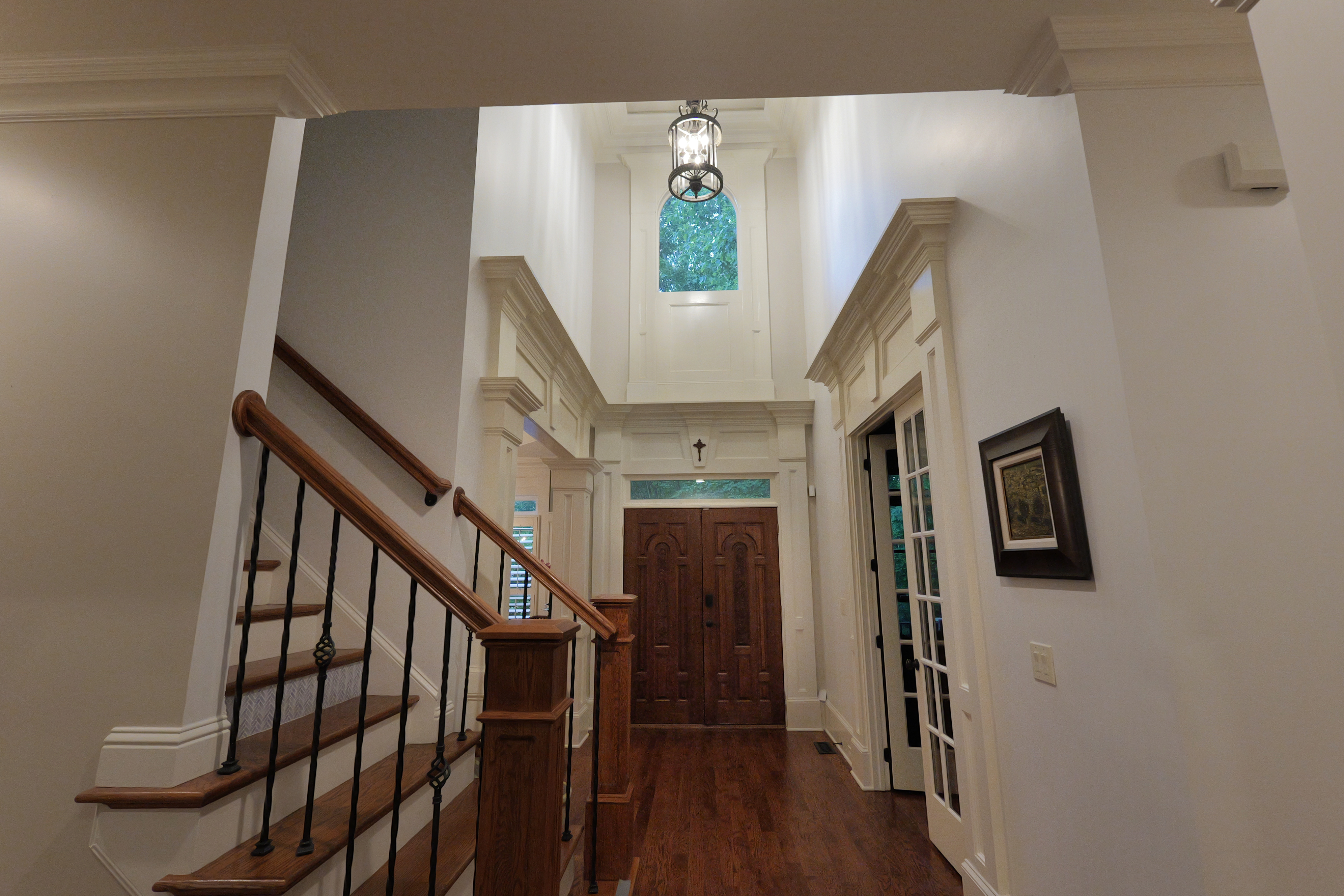Foyer looking back to the front door — two-storey height, lantern pendant, teal transom, carved walnut doors