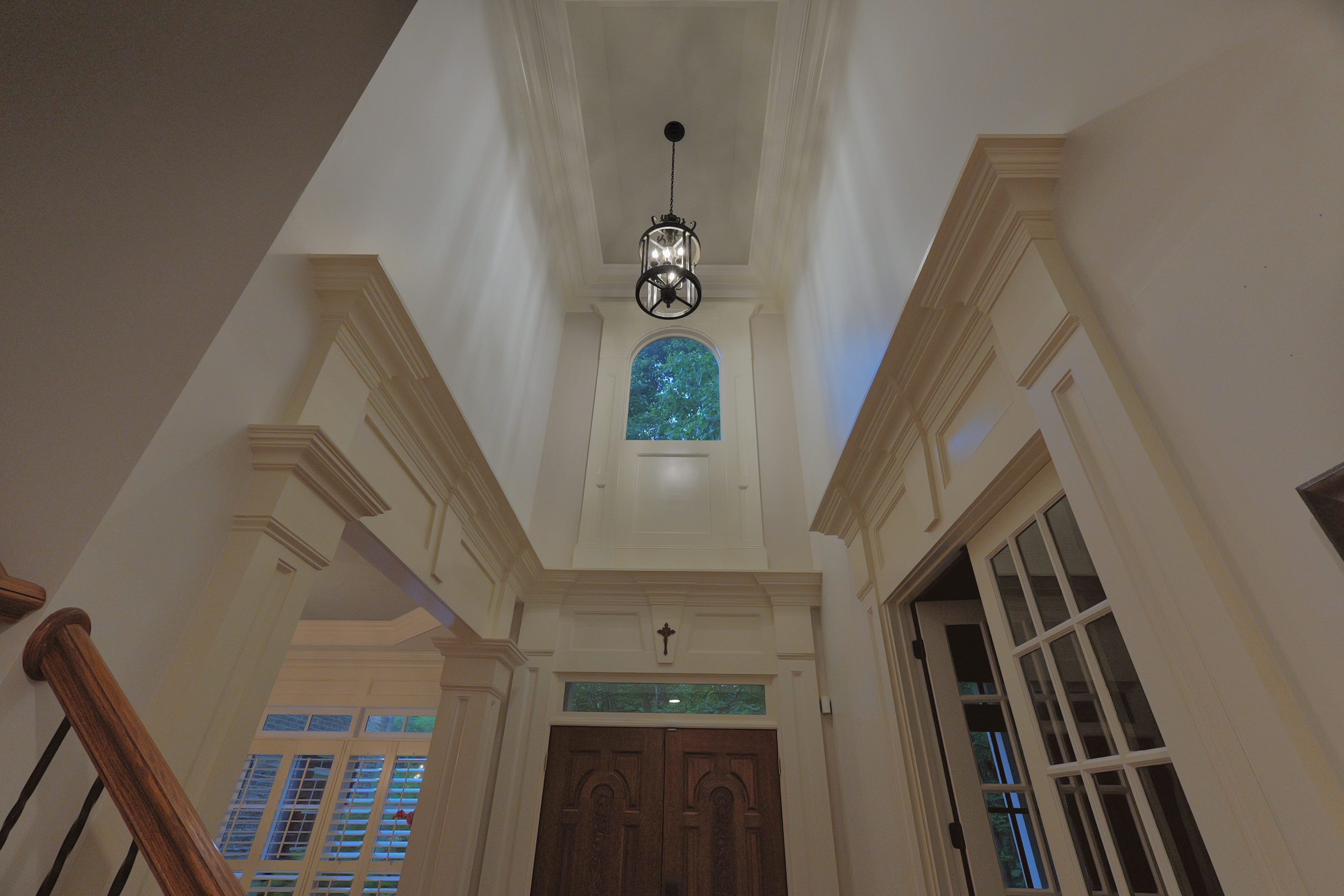 Foyer looking straight up — lantern pendant, arched window, perfect symmetry in two-storey void