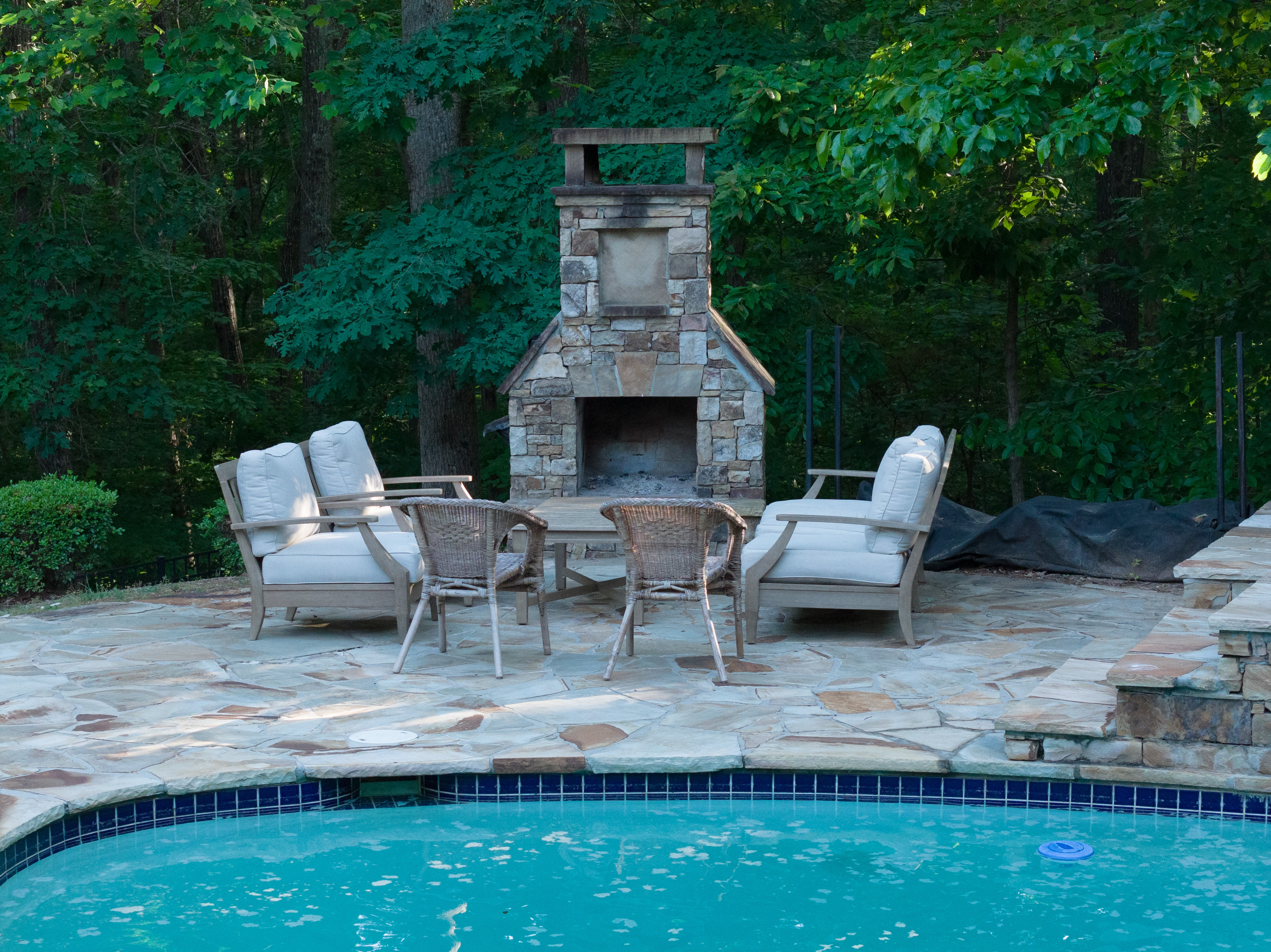 Outdoor stone fireplace and seating viewed from across the pool