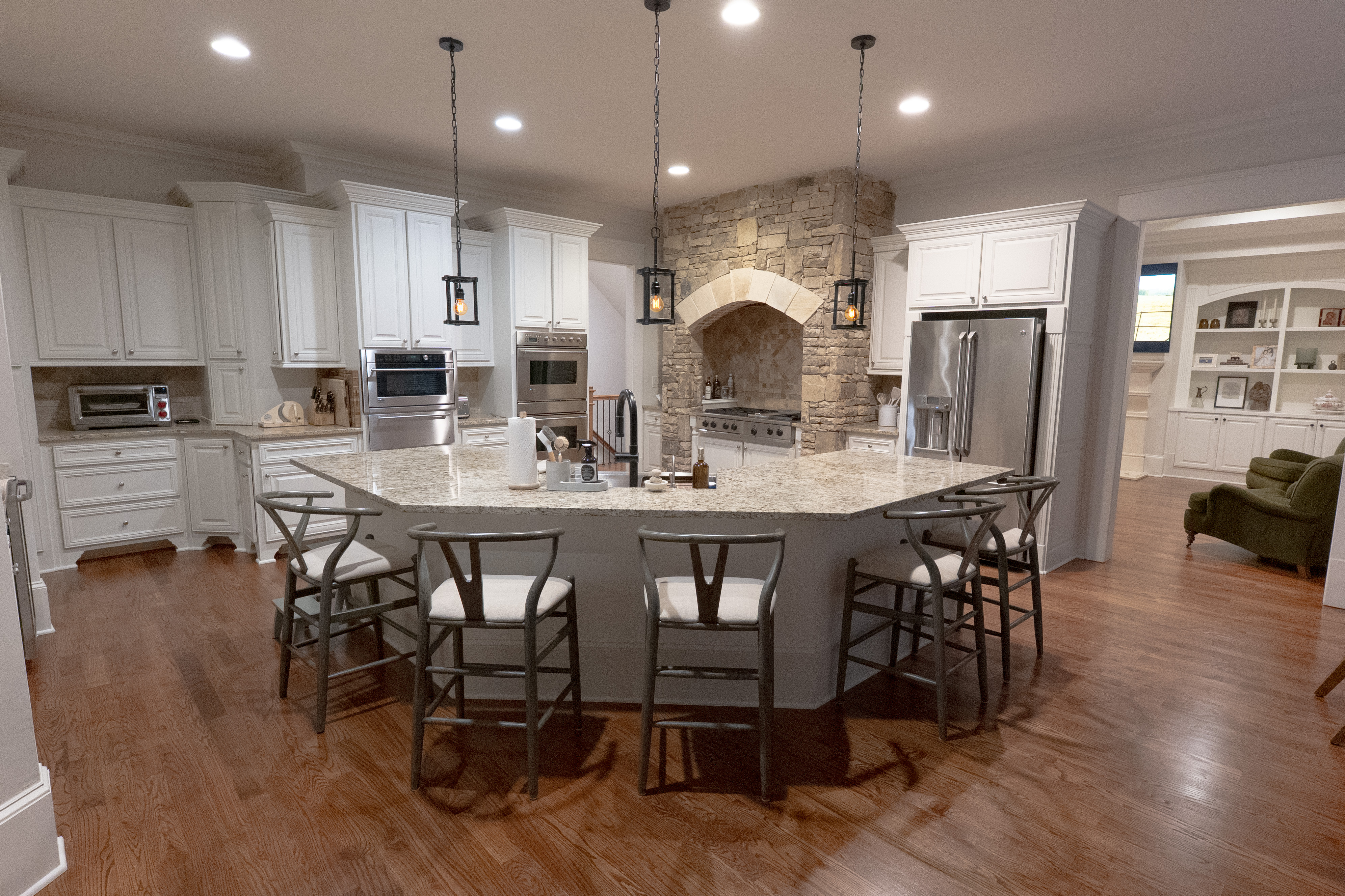 Kitchen island with wishbone bar stools and stone range hood beyond