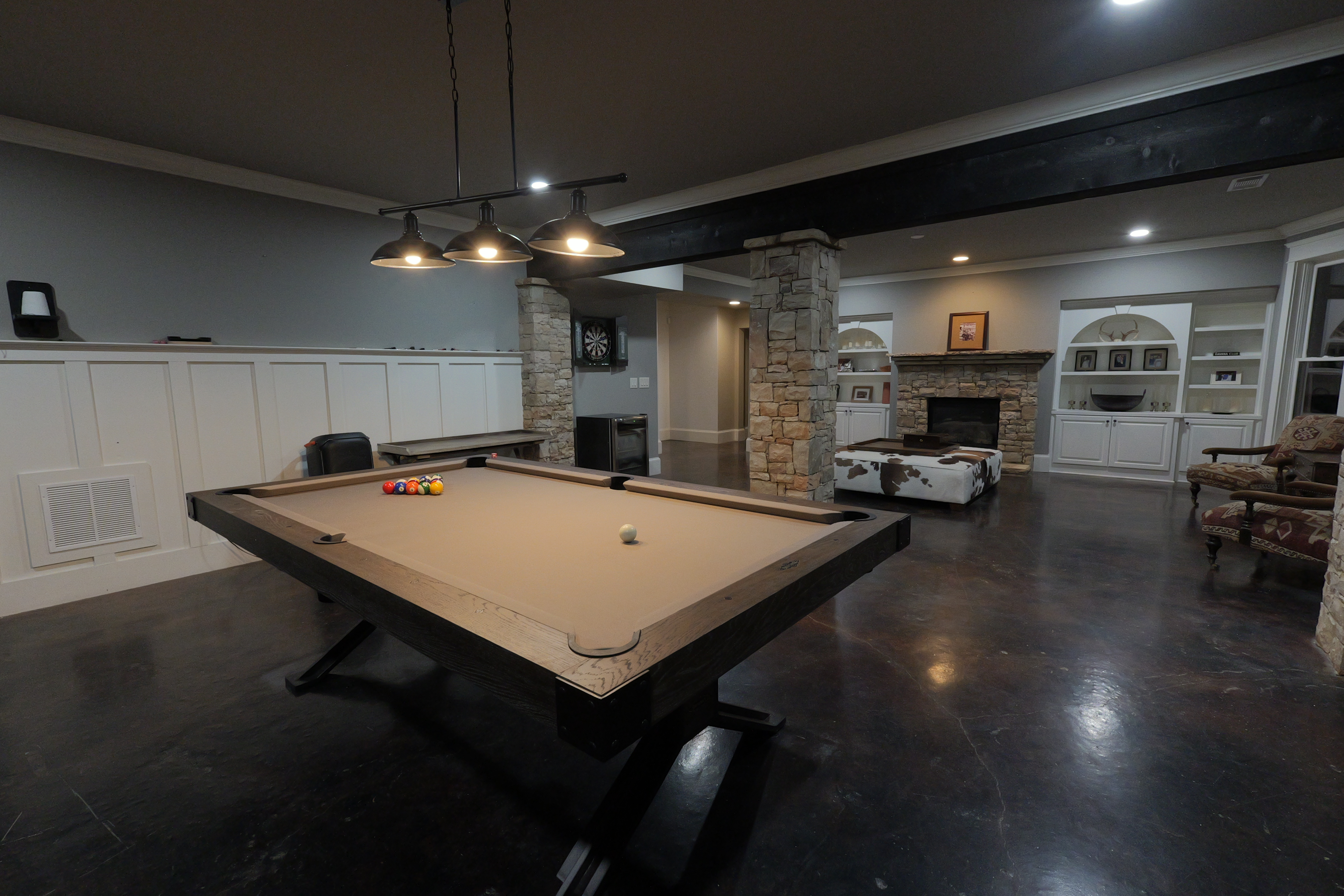 Pool table with triple pendants — stone fireplace and built-ins beyond