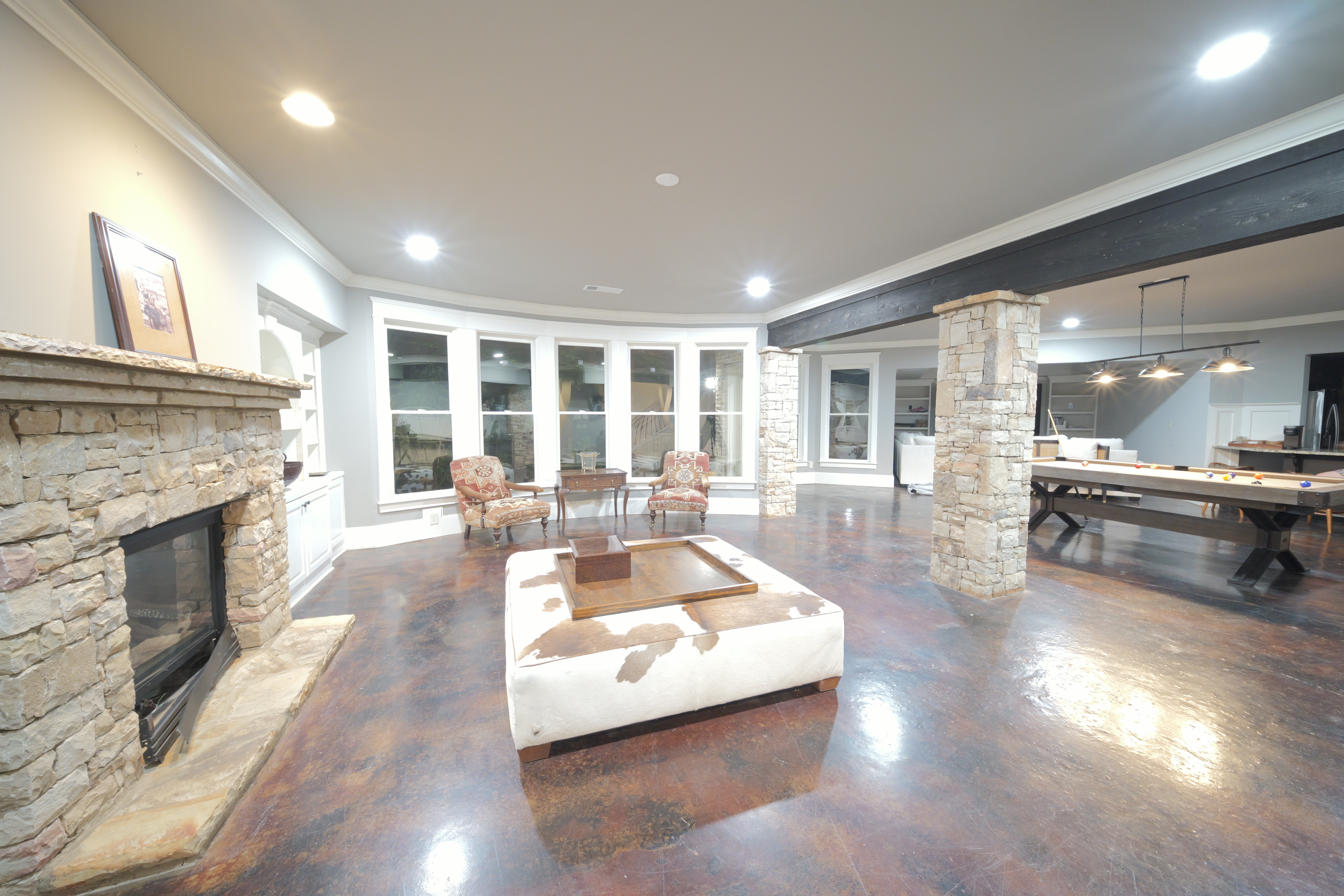 Basement lounge — stone fireplace, cowhide ottoman, stone columns